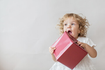 Excited curly girl in white dress with Christmas gift on light gray background 