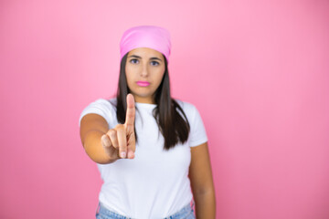 Young beautiful woman wearing pink headscarf over isolated pink background showing and pointing up with fingers number one while is serious
