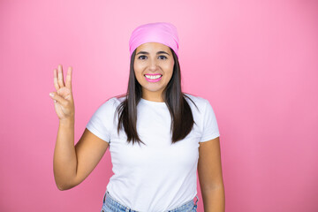 Fototapeta na wymiar Young beautiful woman wearing pink headscarf over isolated pink background showing and pointing up with fingers number three while smiling confident and happy