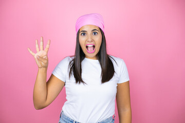 Obraz na płótnie Canvas Young beautiful woman wearing pink headscarf over isolated pink background showing and pointing up with fingers number four while smiling confident and happy