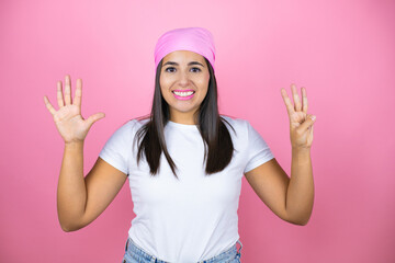Obraz na płótnie Canvas Young beautiful woman wearing pink headscarf over isolated pink background showing and pointing up with fingers number eight while smiling confident and happy