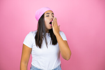 Young beautiful woman wearing pink headscarf over isolated pink background bored yawning tired covering mouth with hand. Restless and sleepiness.