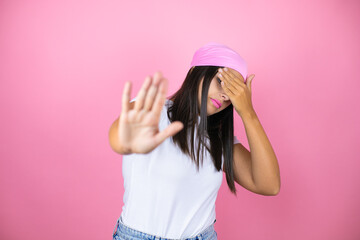 Obraz na płótnie Canvas Young beautiful woman wearing pink headscarf over isolated pink background covering eyes with hands and doing stop gesture with sad and fear expression. Embarrassed and negative concept.