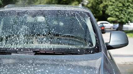 Full car wash at the self service. Splashed drops of water from a sprayer washing the car. Windshield. White foam