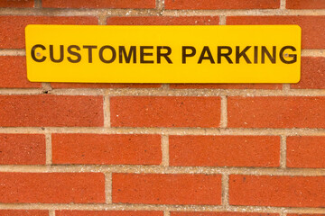 Obraz premium Bright Yellow Customer Parking sign on red brick wall with copy space
