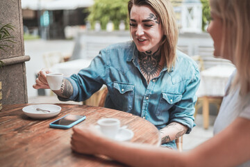 Young alternative women drinking coffee with her friend at bakery bar - Focus on left girl