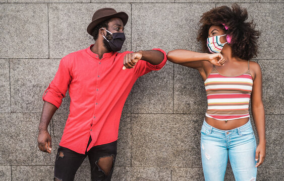 Happy black friends wearing protective masks while bumping their elbows instead of greeting with a hug - Social distance beetween people concept - Focus on faces