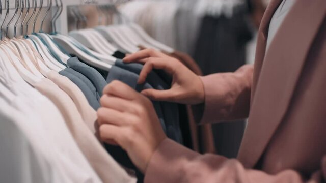 Close up with mid-section of unrecognizable young woman in blazer looking through clothes rack