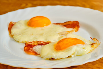 Fried eggs with bacon on white plate