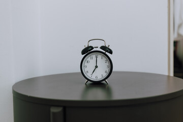 Naklejka premium Old kind of alarm clock on wooden table against blurred white wall, showing 7 a.m