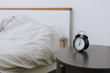 Analog alarm clock on wooden table in bedroom showing 7 a.m time.