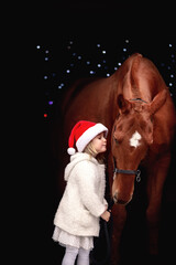 Little beautiful girl posing in christmas outfit next to a big red horse