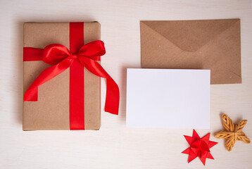 A gift tied with a red ribbon, an envelope from eco paper and a blank sheet for text on a light...