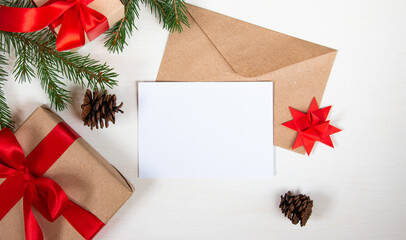 A gift tied with a red ribbon, a spruce branch, an envelope from eco paper and a blank sheet for text on a light background. Christmas and New Year concept. Flat lay, top view.
