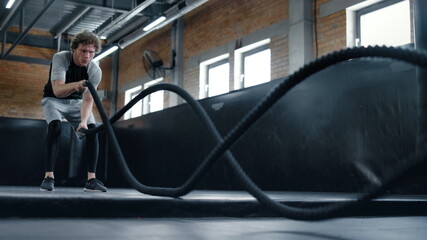 Aggressive kickboxer doing workout at gym. Sportsman using battle ropes