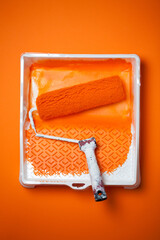 Orange paint roller in tray with orange paint on orange background