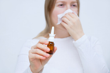 Colds and flu. Caucasian young woman sneezing into a white napkin with  bottle of nasa drops in her hand. Focus on the foreground.