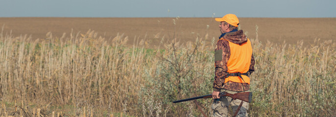 Duck hunter with shotgun walking through a meadow.