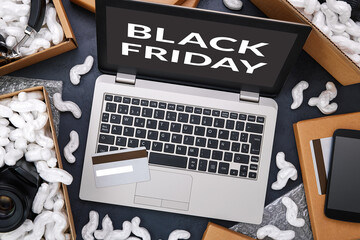 Black Friday and big sale in electronics store concept. Laptop and credit card surrounded by cardboard boxes with protective foam pads and electronic products inside. Flat lay