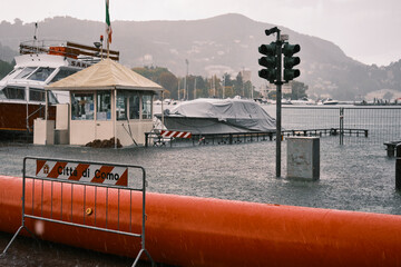 Landscape view of the lakefront of Lake Como flooding out of its boundaries on a storm day. A sign on the street saying "Comune di Como". Lake Como overflowing due to heavy rain