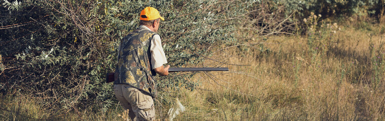 Naklejka premium Duck hunter with shotgun walking through a meadow.