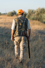 Duck hunter with shotgun walking through a meadow. .Rear view of a man with a weapon in his hands.