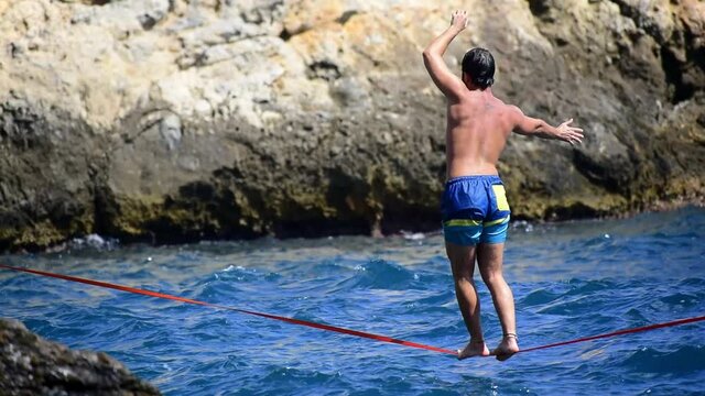 Slacklining sport. Sportsman keeps balance over a slack line. Slackline sport over water. Practice of slack line at mediterranean sea.