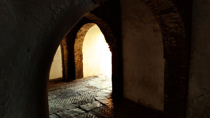 ancient medieval dark passage or corridor with arches in the old town of Seville, Spain, with light at the end of the tunnel