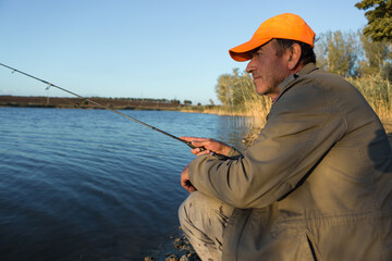 Fishing rod wheel closeup, man fishing with a beautiful sunset.