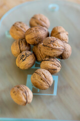 Walnuts on bamboo wooden table in hard shells, pile of dry ripened fruits on glass cutting board, harvested food ingredient