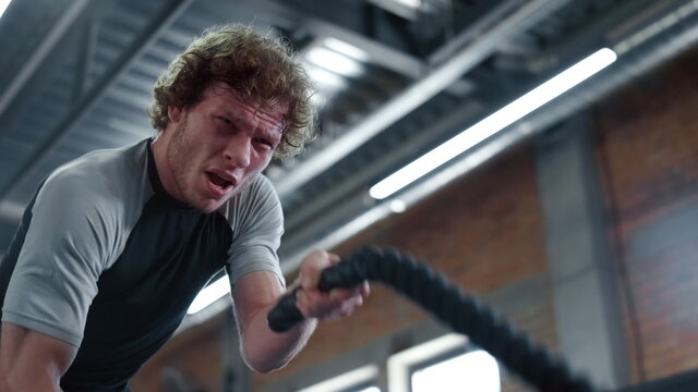 Angry kickboxer training at gym. Fighter using battle ropes in sport club