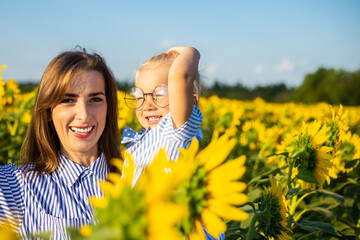 Young woman and a little girl in her arms on a sunflower field. Mum with the child