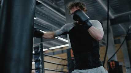 Fototapeta na wymiar Agitated fighter working on blows in fitness center. Sportsman training kicks