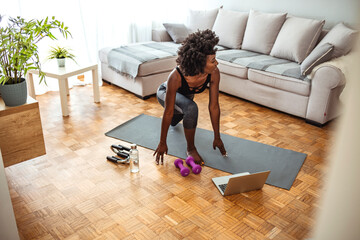 Athletic woman in sportswear doing fitness stretching exercises at home in the living room. Sport and recreation concept. Full length shot of an attractive young woman multitasking