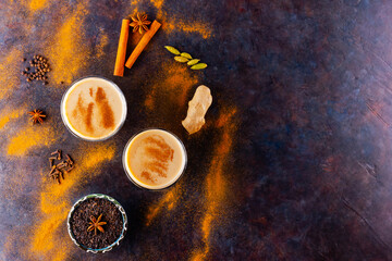 Masala chai tea on a black background. Two transparent glasses of masala tea and scattered various spices. Top view