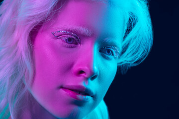 Fairytail. Close up portrait of beautiful albino girl on dark background in neon light. Blonde female model with dreamlike make-up and well-kept skin. Concept of beauty, cosmetics, style, fashion.
