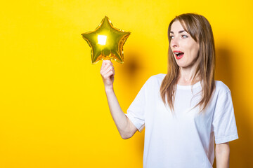 Young woman with a surprised face holds a star balloon in her hands on a yellow background. Banner