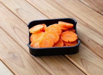 fresh raw carrots sliced on square plate isolated on wooden background, shabu, hot pot ingredients