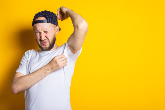 Young man in cap and t-shirt with sweaty and smelly armpits on yellow background