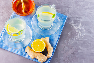 Obraz na płótnie Canvas Ginger tea with lemon on a blue napkin. Two cups of ginger tea, honey and various ingredients. Copy space. Top view