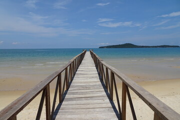 Obraz premium Wooden bridge leading into the ocean across a beach towards an island from Koh Ta Kiev Cambodia