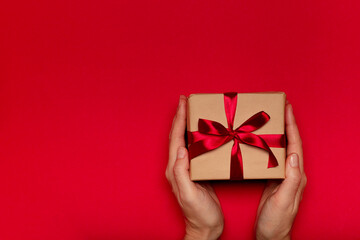 Female's hands holding gift box with red ribbon on red background. Christmas, Valentine's day, New Year and birthday concept, top view
