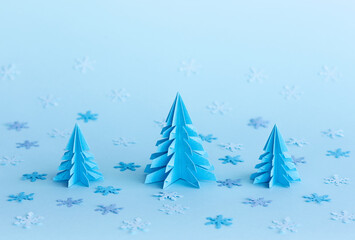 Christmas background. New Year's concept made of paper origami trees on a blue background with snowflakes. Copy space. Paper art. New Year's background with paper fir. Minimal winter holidays idea.