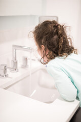 Young girl child toddler brushing her teeth in the bathroom at the basin with a large mirror modern white clean simple bathroom