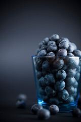 Glass filled with fresh blueberries on dark background. Studio shot. Selective focus on subject.