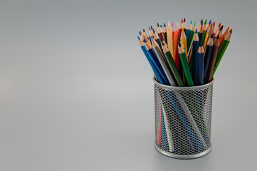 Multi-colored pencils are laid out in a gray metal glass. Side view
