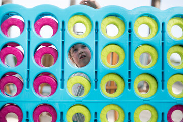 Young girl child face playing large oversize fun connect four game pink blue green circles strategy...