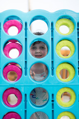 young caucasian girl child face cute smile through gian Connect four game strategy blue green pink...