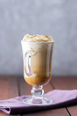 Pumpkin spice latte in a glass mug. Pumpkin latte with whipped cream and spices on a wooden boards. Hot autumn coffee drink on a linen napkin