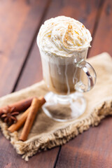 Pumpkin spice latte in a glass mug. Pumpkin latte with whipped cream and spices on a wooden background. Hot autumn coffee drink on a burlap